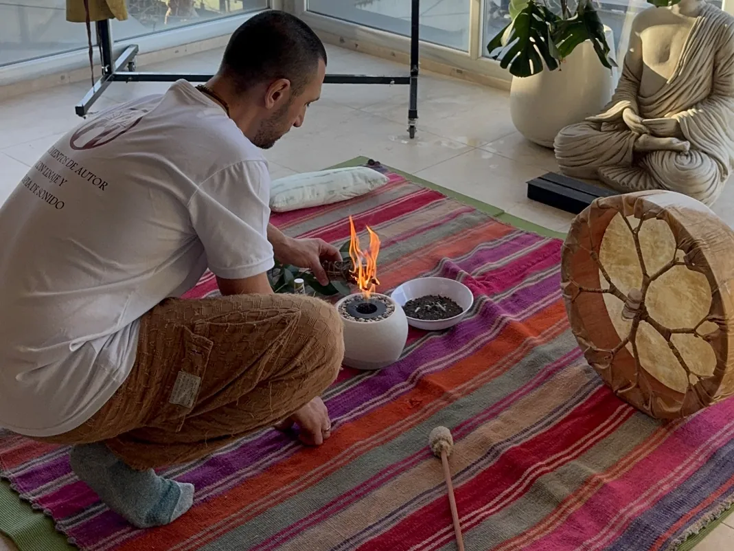 Ra preparando el espacio para un baño de gong: manta de rayas, fuego, tambor y estatua junto a la ventana